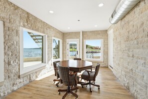 Uma sala de conferências com uma mesa redonda, seis cadeiras e amplas janelas com vista para o mar e um cais.