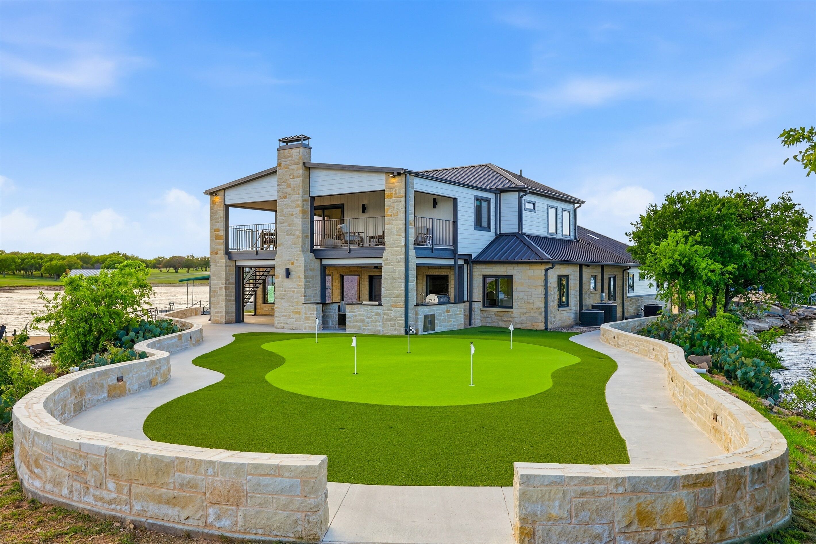 A two-story house with a stone facade, a balcony, and a green lawn with a golf hole.