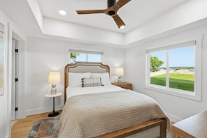 A bedroom with a bed, two bedside tables with lamps, a ceiling fan, a window with a view, and a door. - Point Break at PK Lake- Pickleball, Putting Green and Swim Dock (Graham)