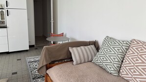 Una habitación pequeña con cama, una mesita redonda, kitchenette y una puerta que da a otra habitación.