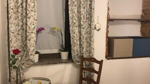 A room with a window, a chair, a small table, a potted plant, and a wall-mounted shelf.