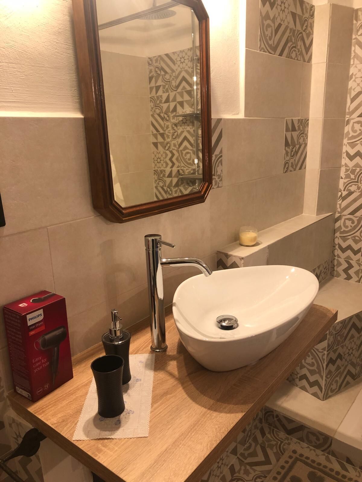 A bathroom with a white sink, a mirror, a Philips hair dryer, and patterned tiles.