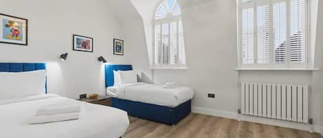 A bedroom with two beds, white bedding, a blue headboard, and a white radiator.