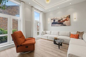 A modern living room with a white sofa, a glass coffee table, and a brown chair. - Stylish London Rental with Sunny Patio (London)