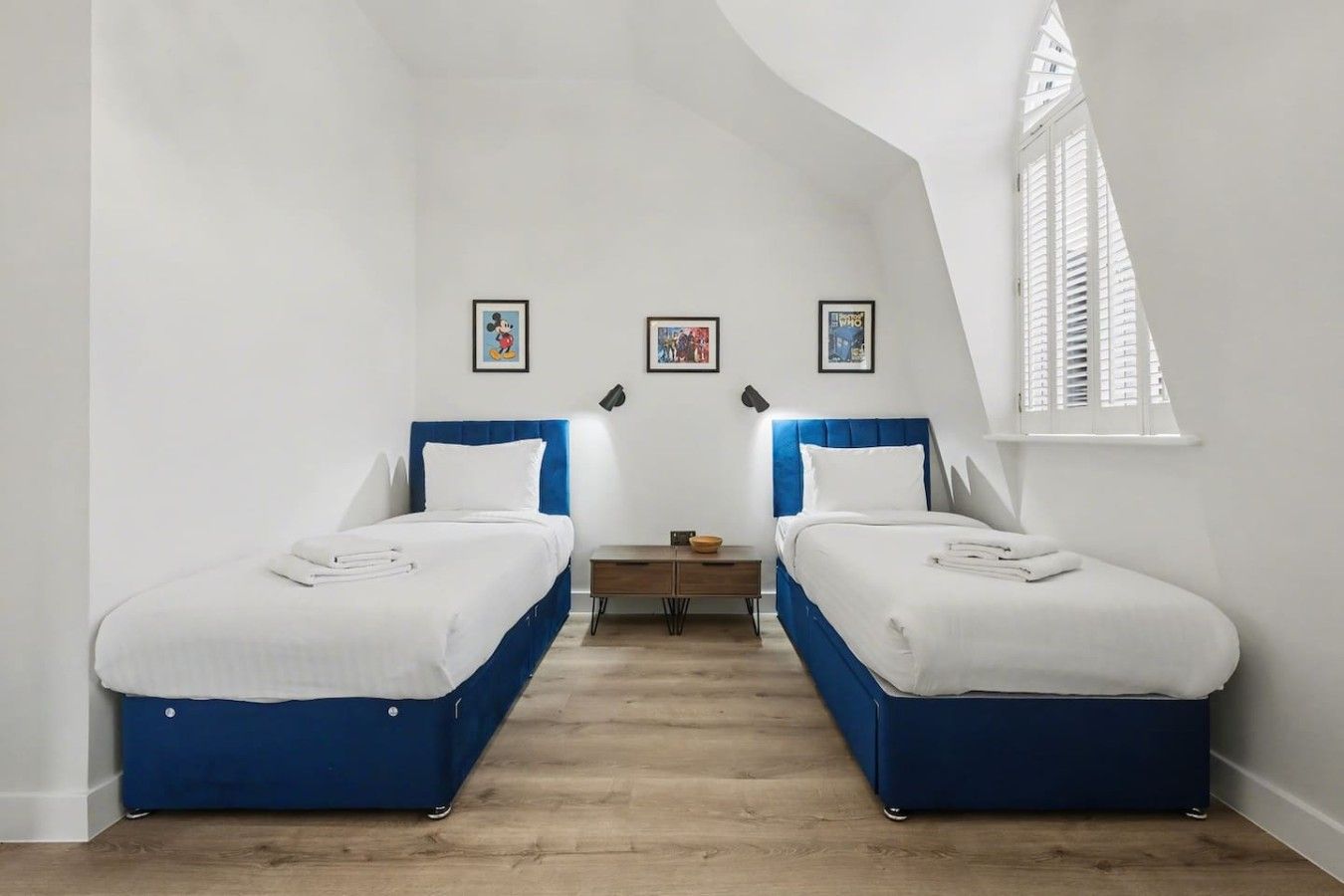 A room with two beds, a small table, and a window with shutters.