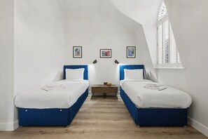 A room with two beds, a small table, and a window with shutters.