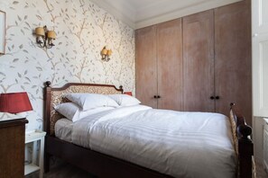 A bedroom with a bed, nightstand, wall-mounted lamps, and a wardrobe. - Chic 1-bed in Notting Hill for 3 (London)