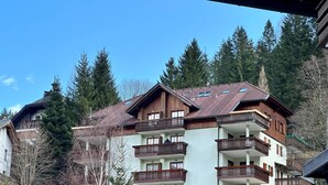 Ein mehrstöckiges Gebäude mit Balkonen, einer Holzfassade und einer Bergkulisse im Hintergrund.