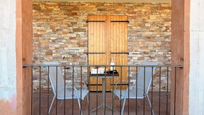 Ein Balkon mit zwei Metallstühlen, einem kleinen runden Tisch und einer Holztür vor einer Steinsandsteinwand.