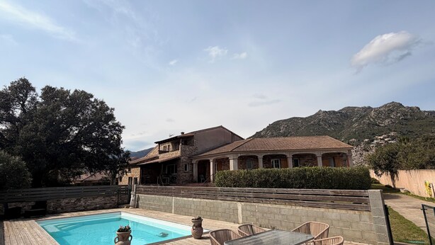 Ein Pool mit Holzterrasse, Steinmauern und Blick auf Berge.
