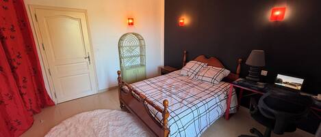 Quarto com cama, escrivaninha com laptop, cadeira, guarda-roupa e cortina vermelha.