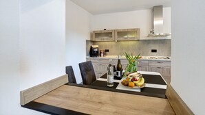 A modern kitchen with a dining area, featuring a black and white table, wooden chairs, a coffee machine, and a fruit bowl.