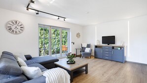 A modern living room with a sofa, a coffee table, a television, and a kitchen area.