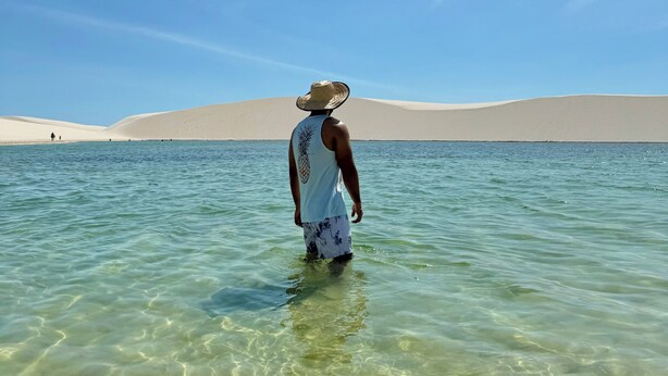 A person standing in clear water with sand dunes in the background.