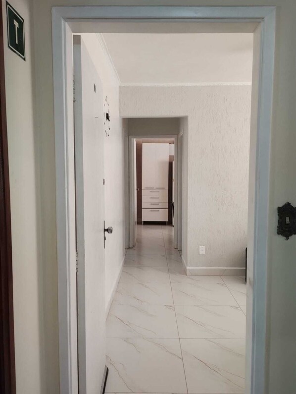 A hallway with a door on the left, a tiled floor, and a view into a room with a cabinet.