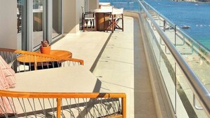 Een balkon met een tafel, stoelen, een bloempot en uitzicht op zee en een rotsachtige kustlijn.