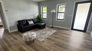 Una sala de estar con un sofá modular, un otoman con estampado, una lámpara de pie y un ventanal grande.