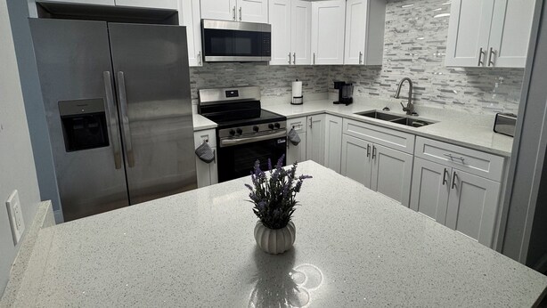 Una cocina moderna con electrodomésticos de acero inoxidable, armarios blancos y encimera de granito.