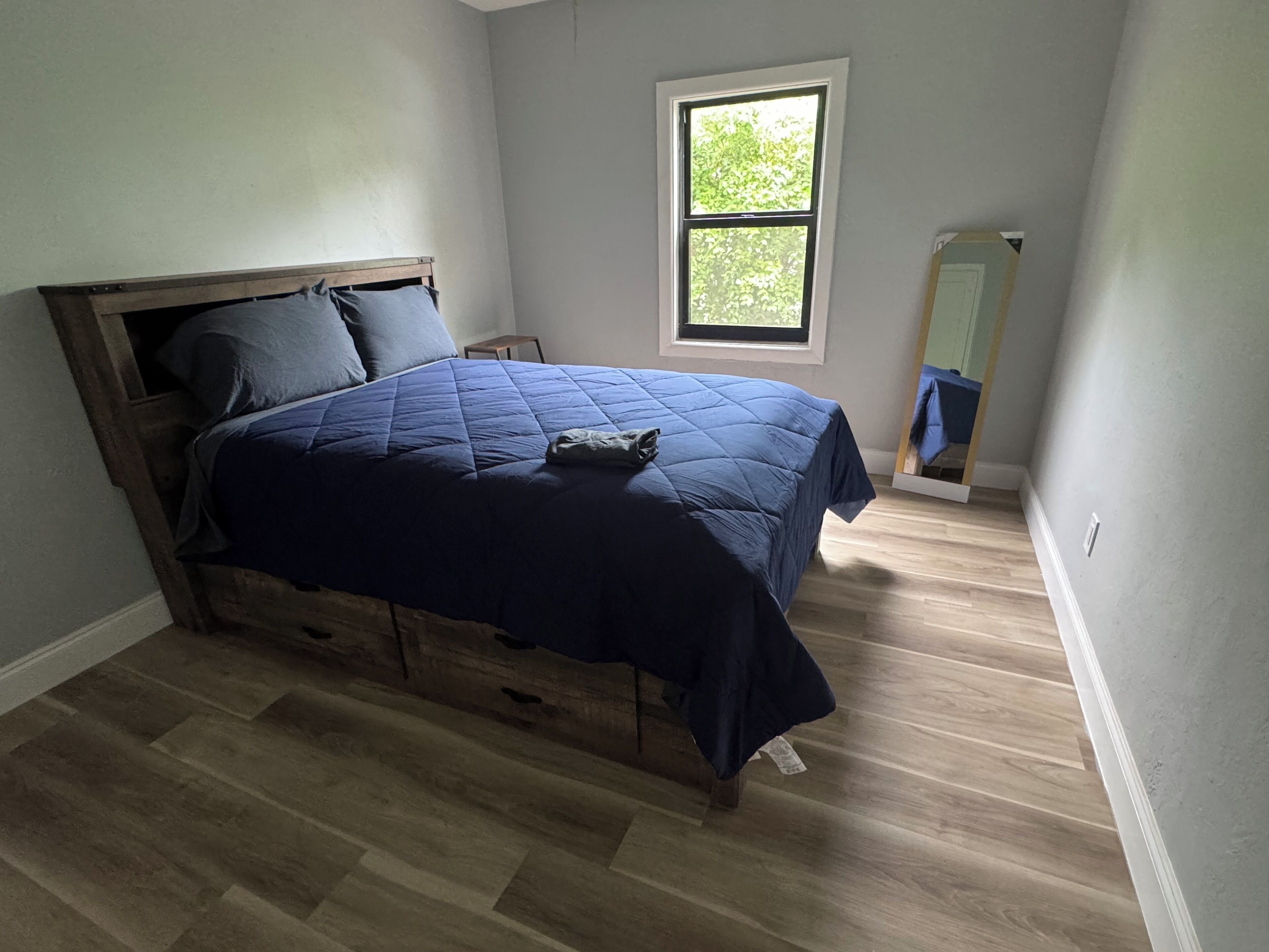 Een slaapkamer met een bed, een raam, een spiegel en een dressoir.