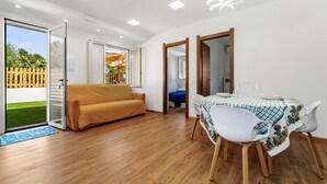 Une pièce moderne avec un plancher en bois, un canapé, une table à manger avec des chaises et une porte-fenêtre coulissante donnant sur un jardin.