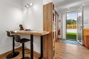 A room with a wooden desk, two black chairs, a fire extinguisher, a sliding glass door to a balcony, and a blue mat on the floor.