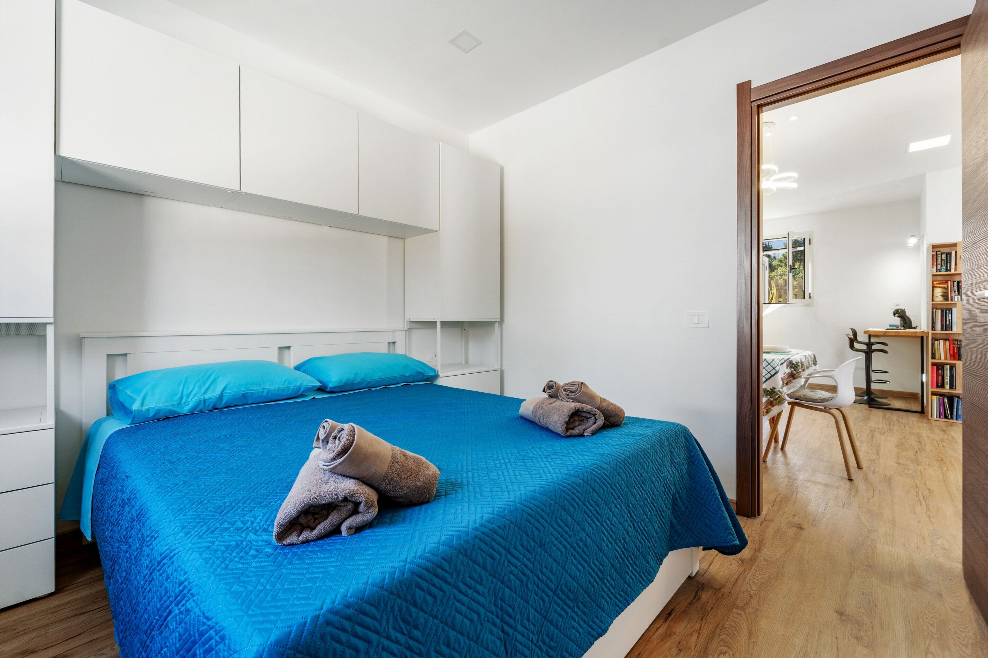 Une chambre moderne avec un grand lit, un plancher en bois et une vue sur une autre pièce où se trouvent un bureau et une chaise.