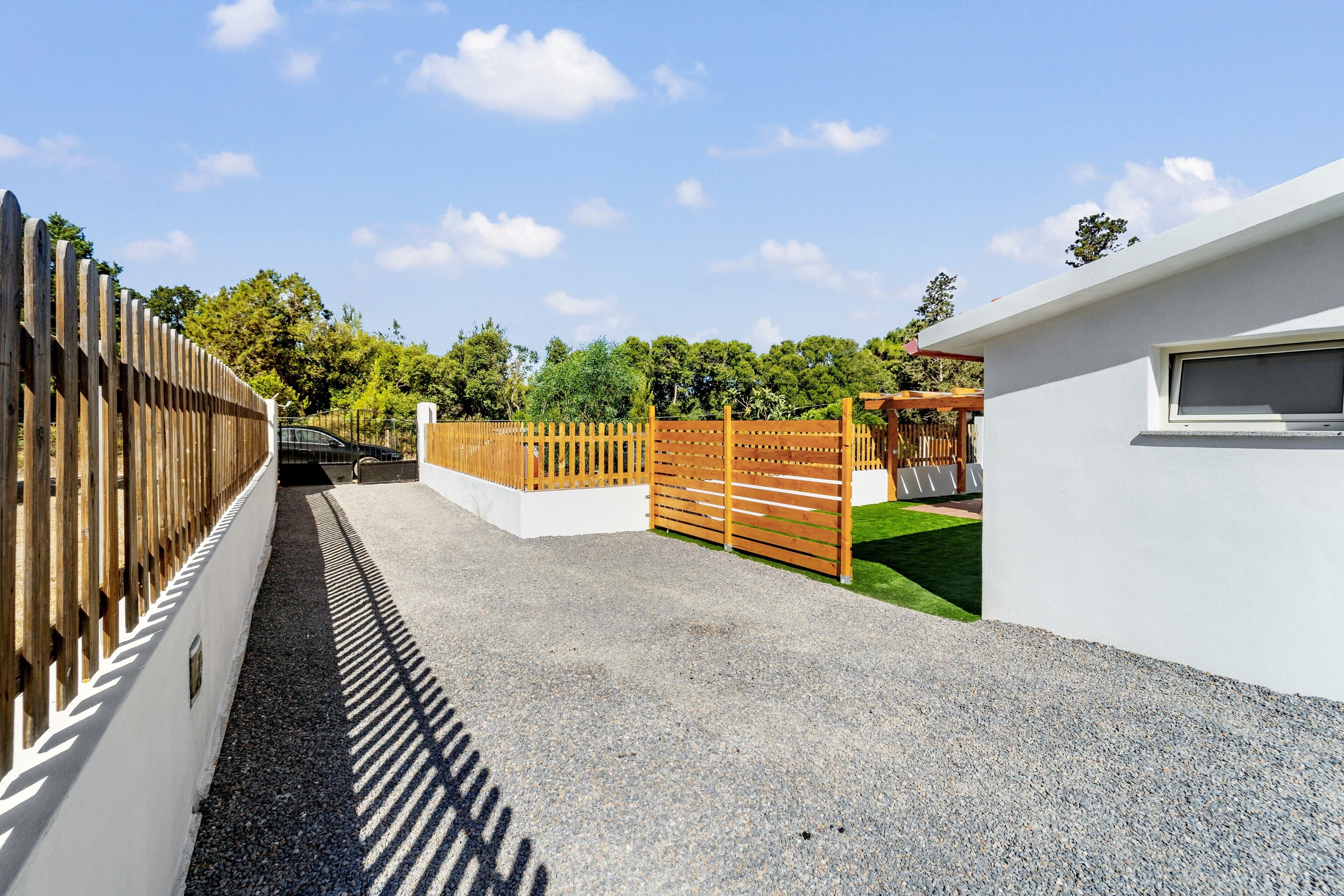 A gated driveway leading to a building with a white exterior and a window.