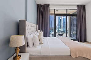 A modern hotel room with a large bed, a bedside lamp, and a view of the cityscape through large windows. - Downtown 1BR with Balcony Near Burj Khalifa & Dubai Mall (Downtown Dubai)