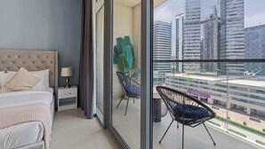 Une chambre d’hôtel moderne avec un grand lit, une table de chevet, une chaise et un balcon offrant une vue sur la ville.