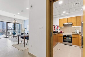 A modern kitchen with wooden cabinets, a stainless steel oven, and a city view through large windows. - Downtown 1BR with Balcony Near Burj Khalifa & Dubai Mall (Downtown Dubai)