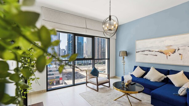 Un salon moderne avec une grande fenêtre, un canapé bleu, une table basse ronde et une vue sur la ville.