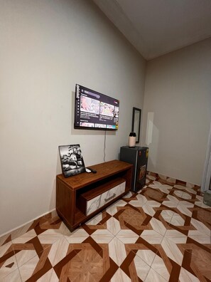 A room with a flat-screen TV mounted on the wall, a wooden cabinet with a drawer, and a patterned floor. - Private Room Ensuite with AC at Pokuase- Mayera Road (Mayera)