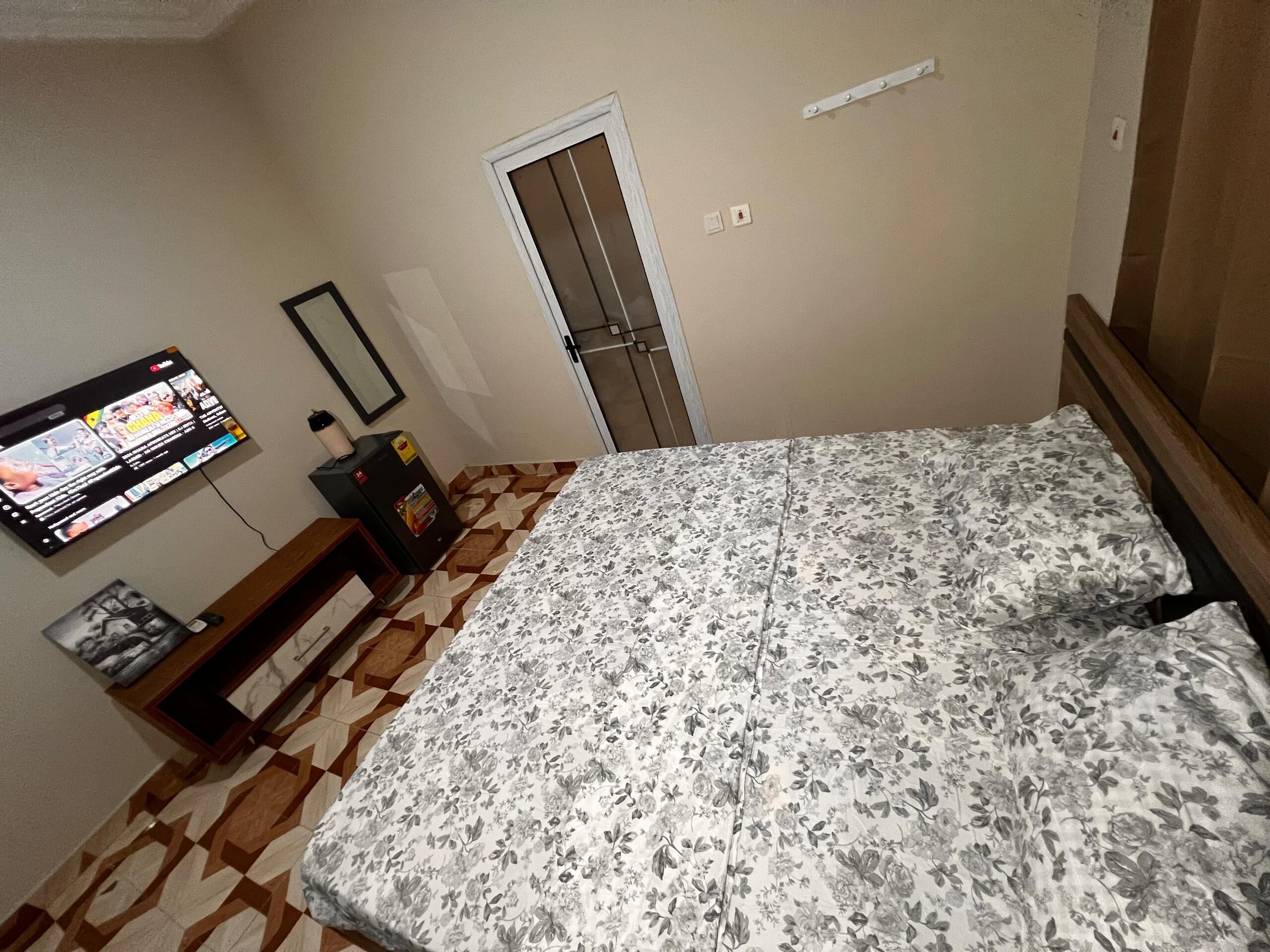 Ein Schlafzimmer mit einem Bett, einem an der Wand befestigten Fernseher, einer Tür und einem gemusterten Boden.