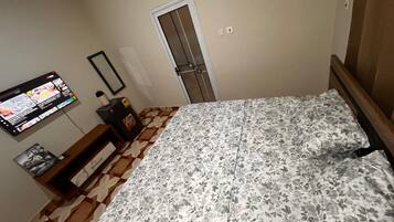 A bedroom with a bed, a TV mounted on the wall, a door, and a patterned floor.