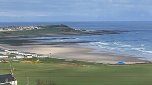Un paysage côtier comprenant une plage, des zones herbeuses et un petit bâtiment.