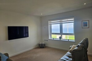 A room with a large window, a flat-screen TV mounted on the wall, and a grey sofa.