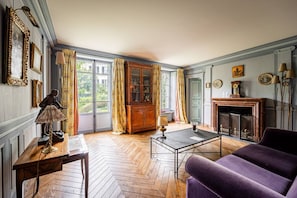 A room with a herringbone floor, a purple sofa, a wooden cabinet, and a fireplace. - 4 bedrooms/Castle/Garden/Montmartre (Paris)
