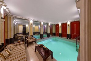 Een hotelkamer met een groot zwembad, spiegelende muren en een bank.