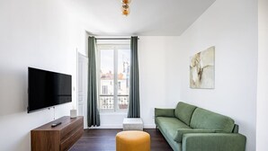En moderne stue med et fladskærms-tv, en grøn sofa, et træsidebord og en gul fodskammel.