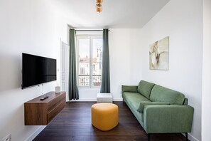 A modern living room with a flat-screen TV, a green sofa, a wooden side table, and a yellow ottoman. - Apartment 2 Bedrooms#2 Bathrooms#Paris 14#Alesia (Paris)