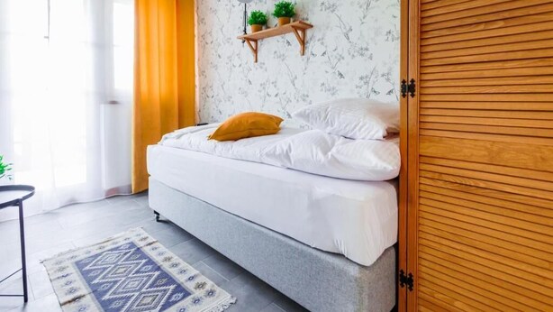 A bedroom with a bed, a wooden wardrobe, a shelf with plants, a clock, and a patterned rug. - Panorama Górska Wisła Resort & SPA (Wisła)
