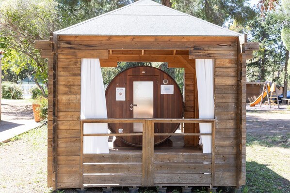A wooden cabin with a door, a small porch, and a slide in the background. - Bungalow “Village Camping De L'Ostriconi G3” with Sea View, Shared Pool and Wi-Fi (Palasca)