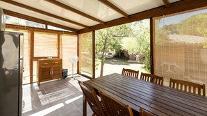 Eine überdachte Terrasse mit Holztisch und -stühlen, einem kleinen Schrank und einem Ventilator.