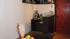 Ein Zimmer mit Tisch, dekoriert mit einer Vase und Früchten, einer Kaffeemaschine und einem Regal mit Flaschen.