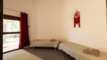 A room with two beds, a window with red curtains, a dreamcatcher, and a view of greenery outside.