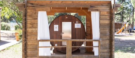 Een houten hut met een deur, een klein terras en een glijbaan op de achtergrond.