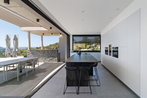 A modern kitchen with a large island, bar stools, and a view of the outdoors. - Villa "Alba" with Sea View, Wi-Fi, and Air Conditioning (Zonza)