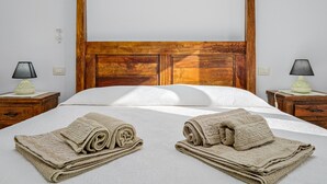 A hotel room with a wooden headboard, two bedside tables with lamps, a neatly made bed with rolled towels, and a white wall. - Apartment 'Bella Vista Su Tavolara 4' with Tavolara View, Wi-Fi and Air Conditioning (Porto San Paolo)