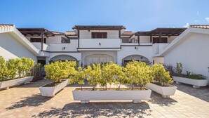 A courtyard with a building featuring a central arched entrance, surrounded by potted plants and a tiled floor. - Apartment 'Bella Vista Su Tavolara 4' with Tavolara View, Wi-Fi and Air Conditioning (Porto San Paolo)