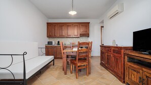 A compact kitchen with wooden cabinets, a dining table, chairs, a TV, and a microwave. - Apartment 'Bella Vista Su Tavolara 4' with Tavolara View, Wi-Fi and Air Conditioning (Porto San Paolo)